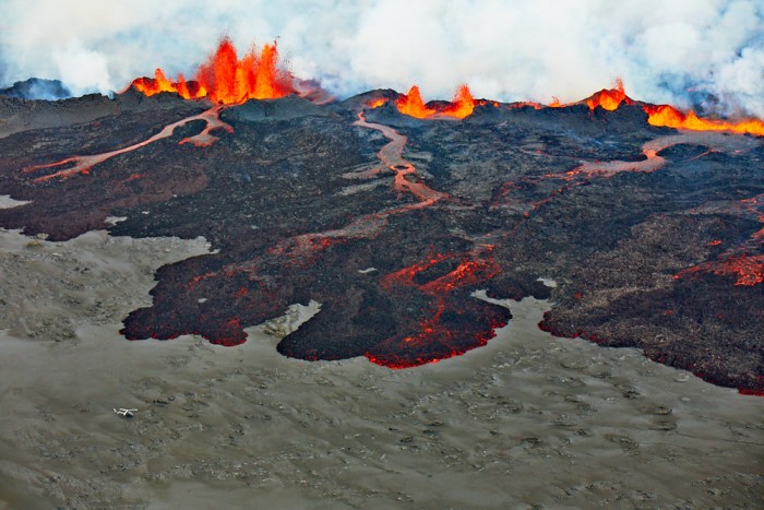 Spalte die Lava Spuckt Und Fliessende, glühende Lava. Links Unten im Bild ein Helikopter Und drei Personen